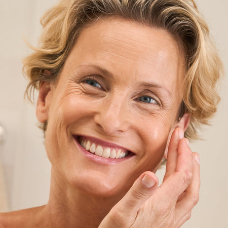 Smiling woman applying Tropic Skincare product to her face, showcasing healthy and radiant skin.